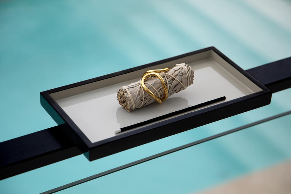A bundle of white sage placed in a gold-ornate, black and white tray with a serene water background.